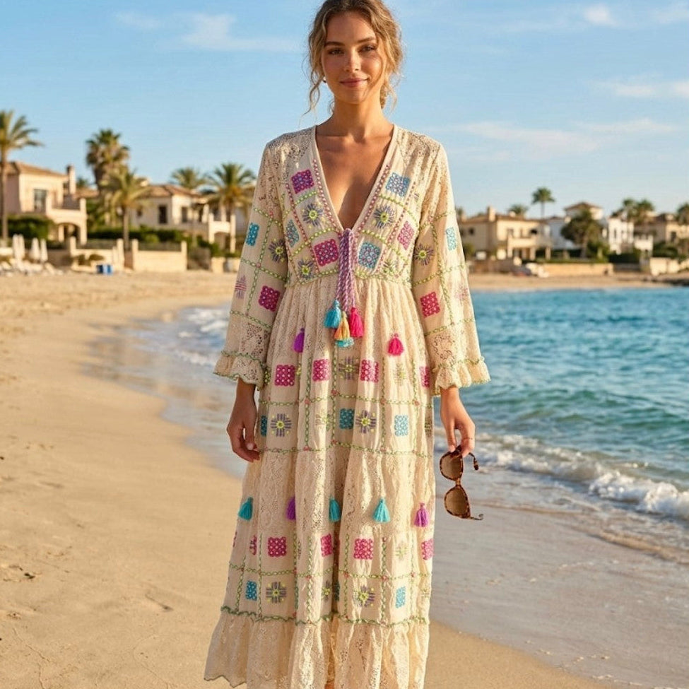 Woman in a patterned dress standing on a beach with palm trees and buildings in the background.
