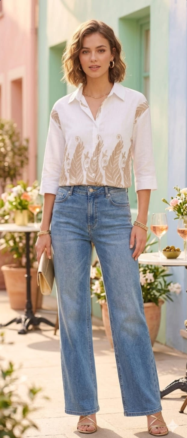 Woman wearing a white blouse and blue jeans standing outdoors with colorful buildings in the background.